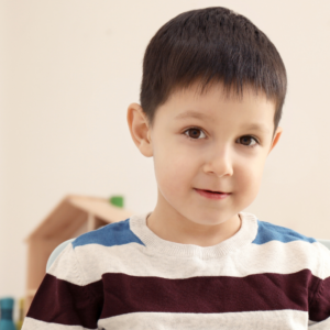 Lewis is a white six-year-old boy with dark short hair wearing a stripy jumper and half smiling