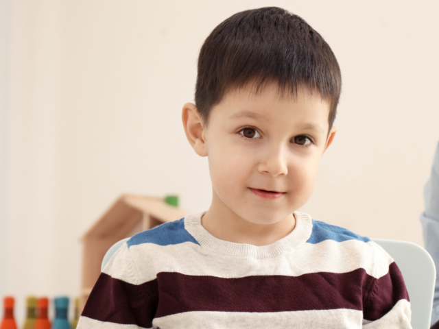 Lewis is a white six-year-old boy with dark short hair wearing a stripy jumper and half smiling