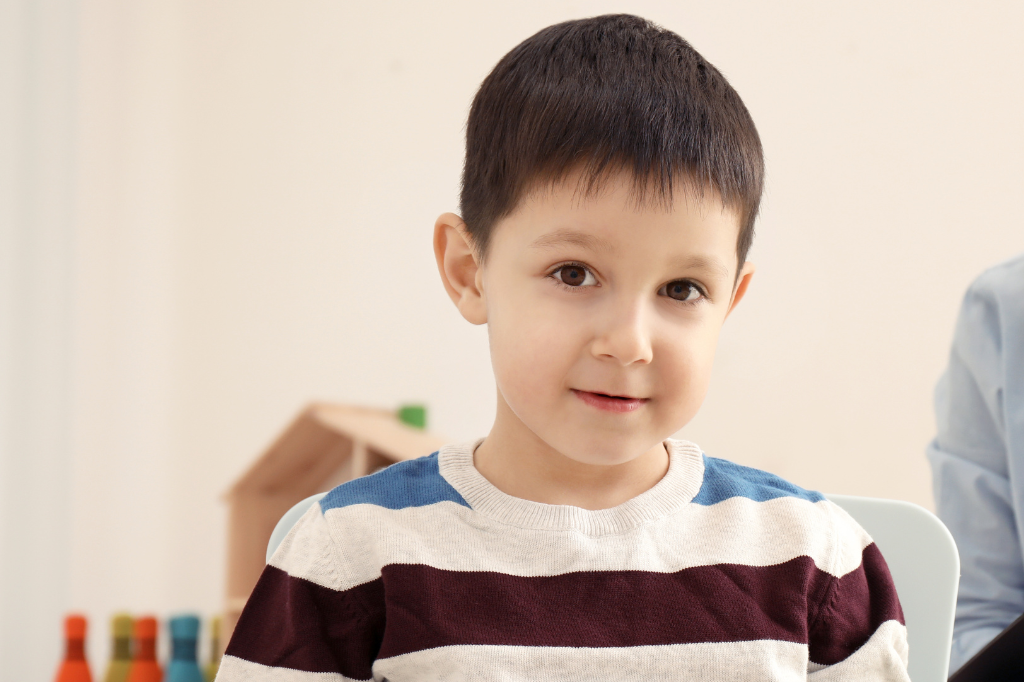 Lewis is a white six-year-old boy with dark short hair wearing a stripy jumper and half smiling