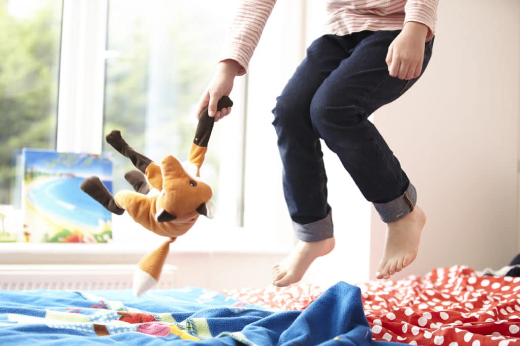 Girl jumping on a bed with a teddy