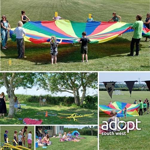 A group of children and adults playing with a rainbow parachute or amidst trees.